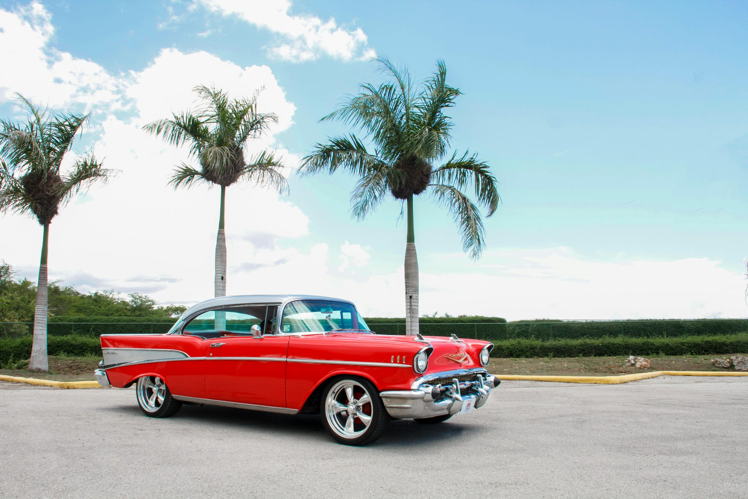 red muscle car parked next to three palm trees